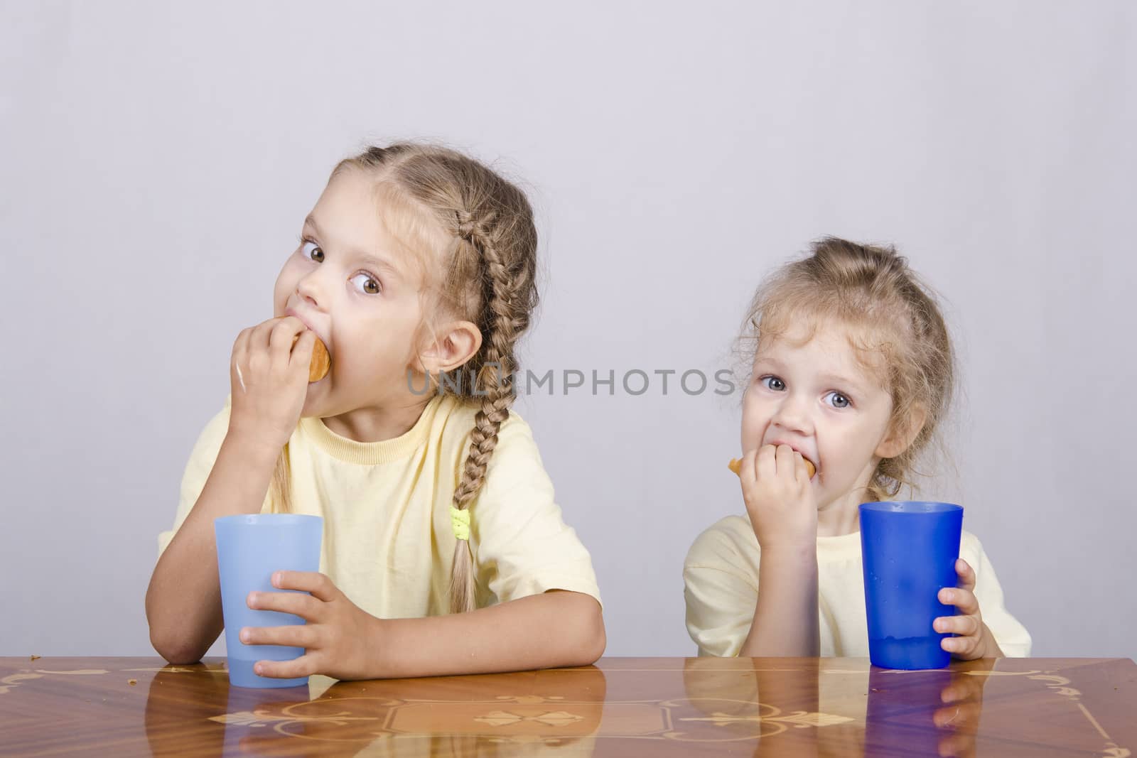 Two children sitting at the table, eating a muffin and drink of colored plastic cups