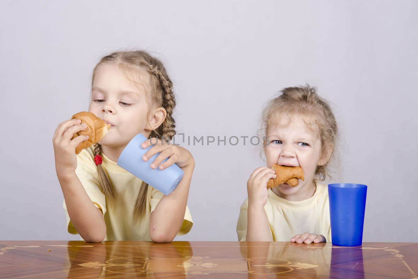 Two children sitting at the table, eating a muffin and drink of colored plastic cups