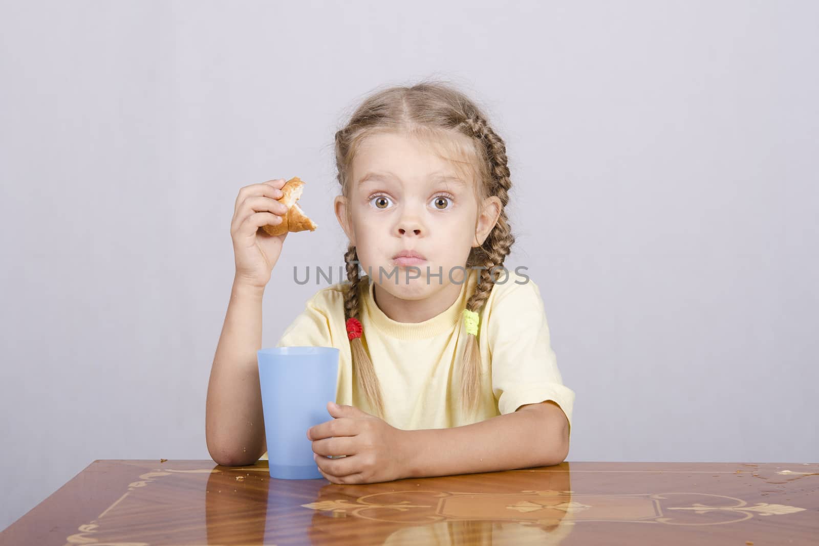 Four-year-old girl sitting at the table, eating a muffin and drinking from a plastic Cup