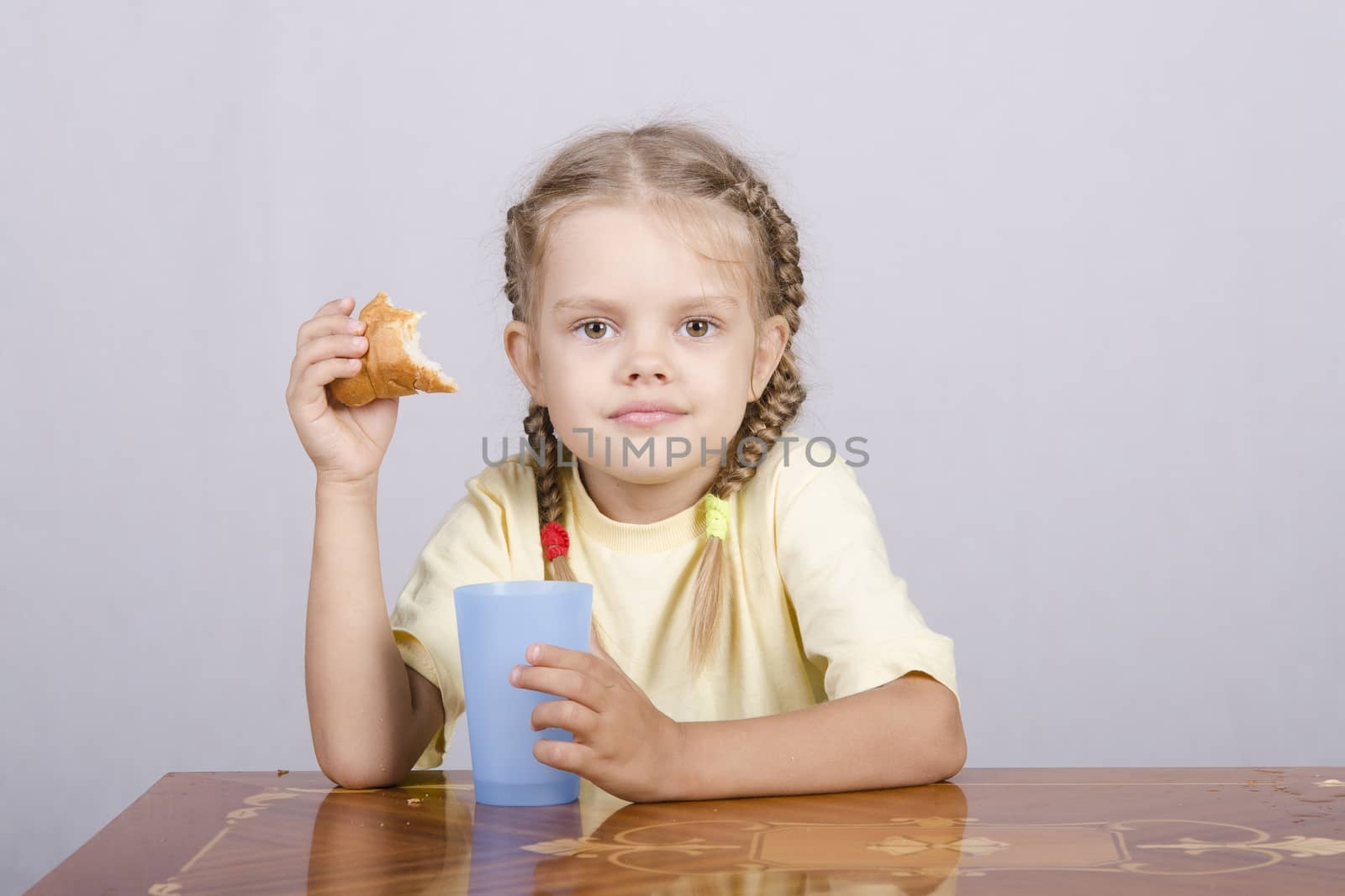 Four-year-old girl sitting at the table, eating a muffin and drinking from a plastic Cup