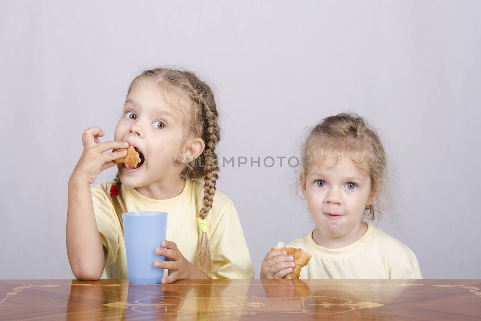 Two children sitting at the table, eating a muffin and drink of colored plastic cups