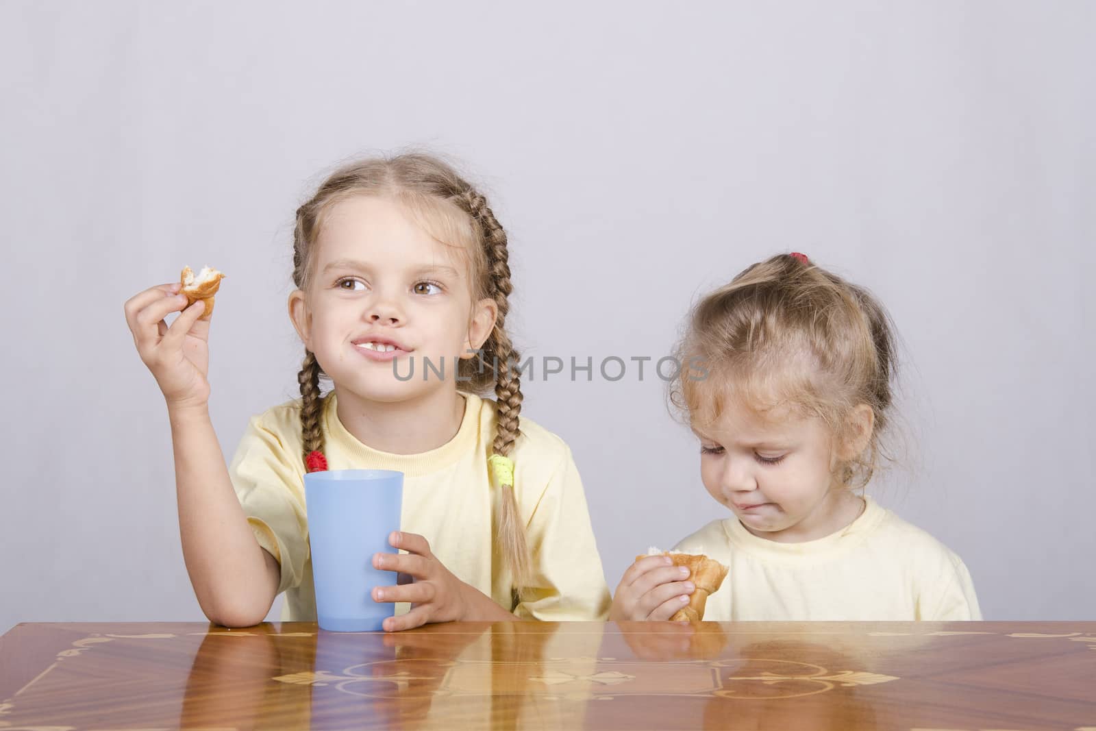 Two children sitting at the table, eating a muffin and drink of colored plastic cups