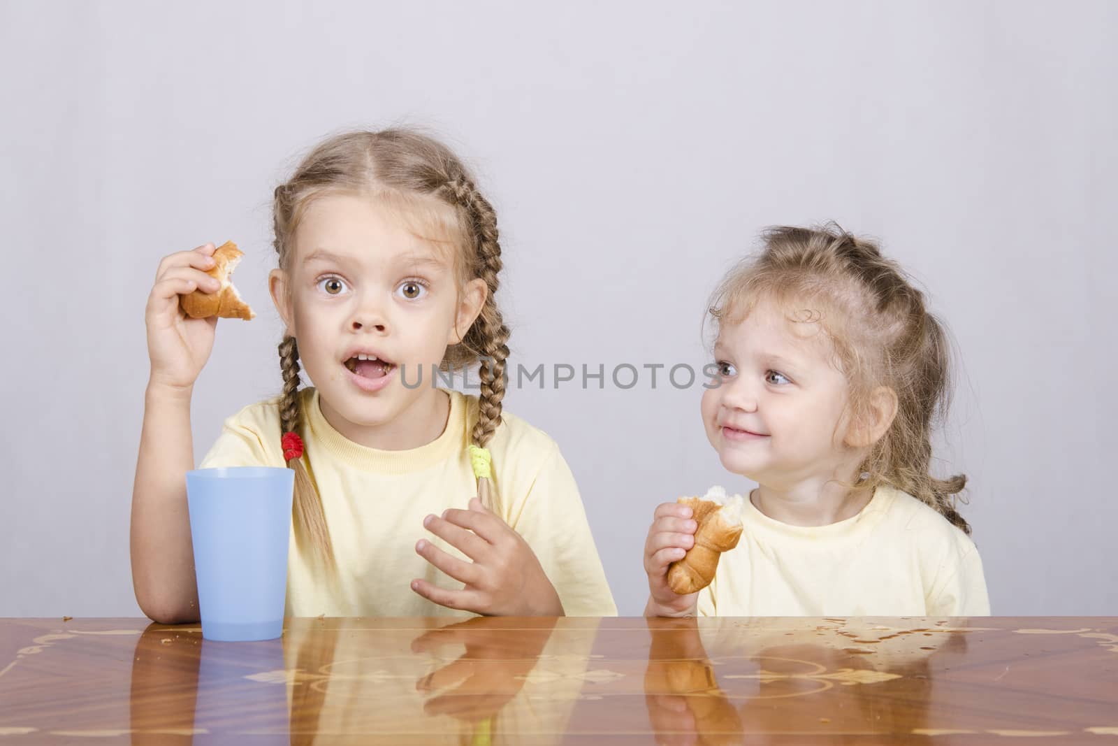 Two children sitting at the table, eating a muffin and drink of colored plastic cups