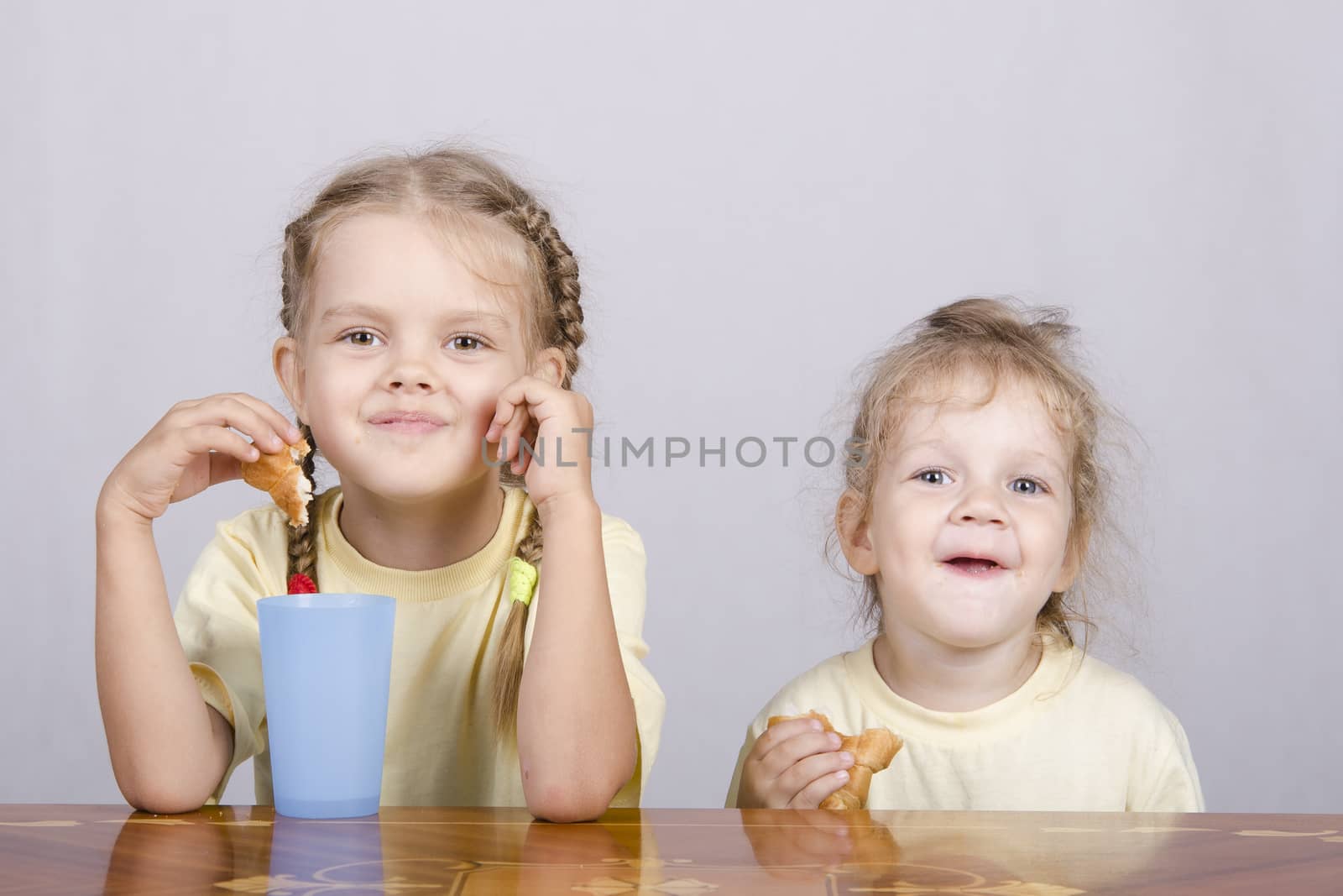 Two children sitting at the table, eating a muffin and drink of colored plastic cups