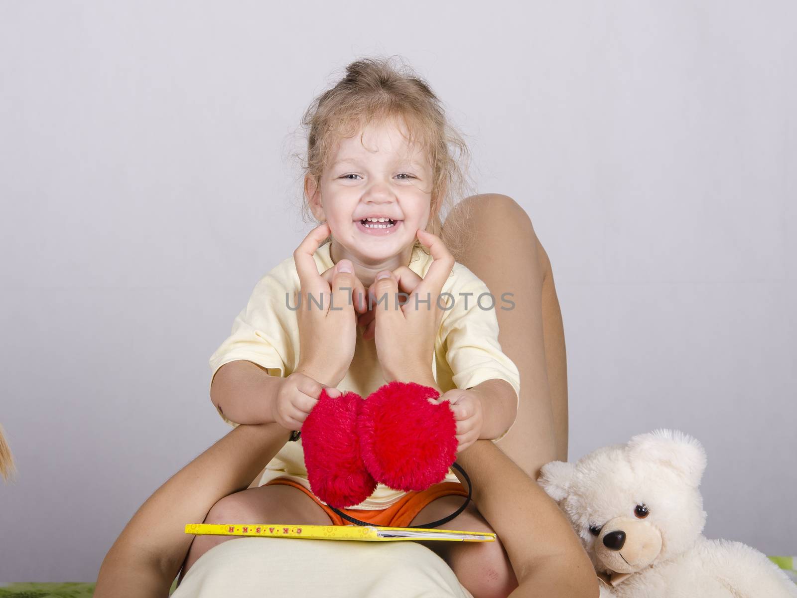 Little girl sitting on my mom with headphones and a book. Mom tickles the girl, smiling girl