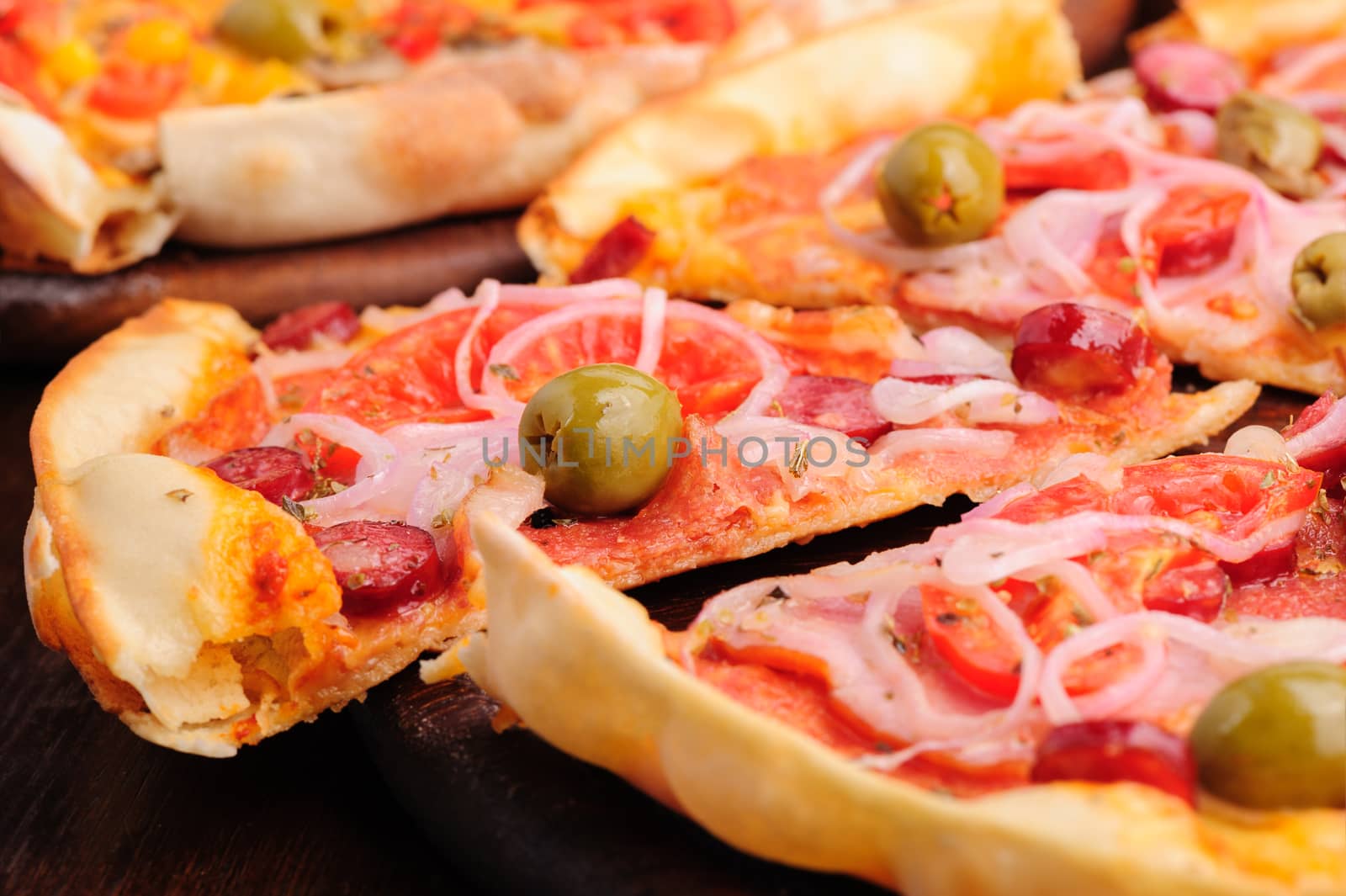 Closeup of pizza with tomato, salami, peppeeoni, olives and yellow hot pepper