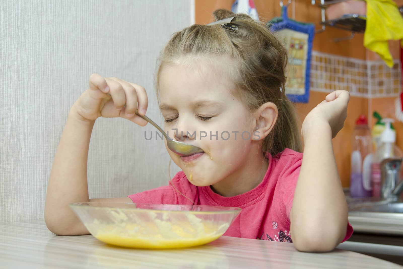 Girl five years eats porridge, sitting at the kitchen table.