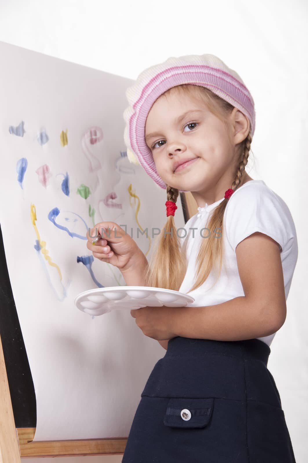 Four-year-old girl playing in the artist and draws on the easel-painting. In the arms of children brush and palette.