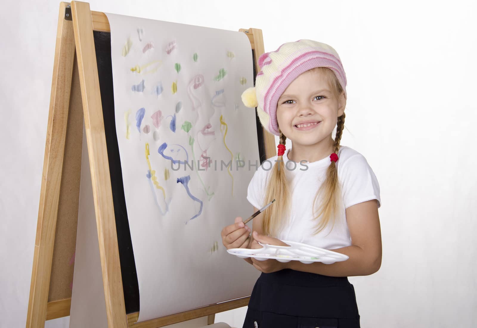 Four-year-old girl draws on the easel-painting. In the arms of children brush and palette. Light background, Studio