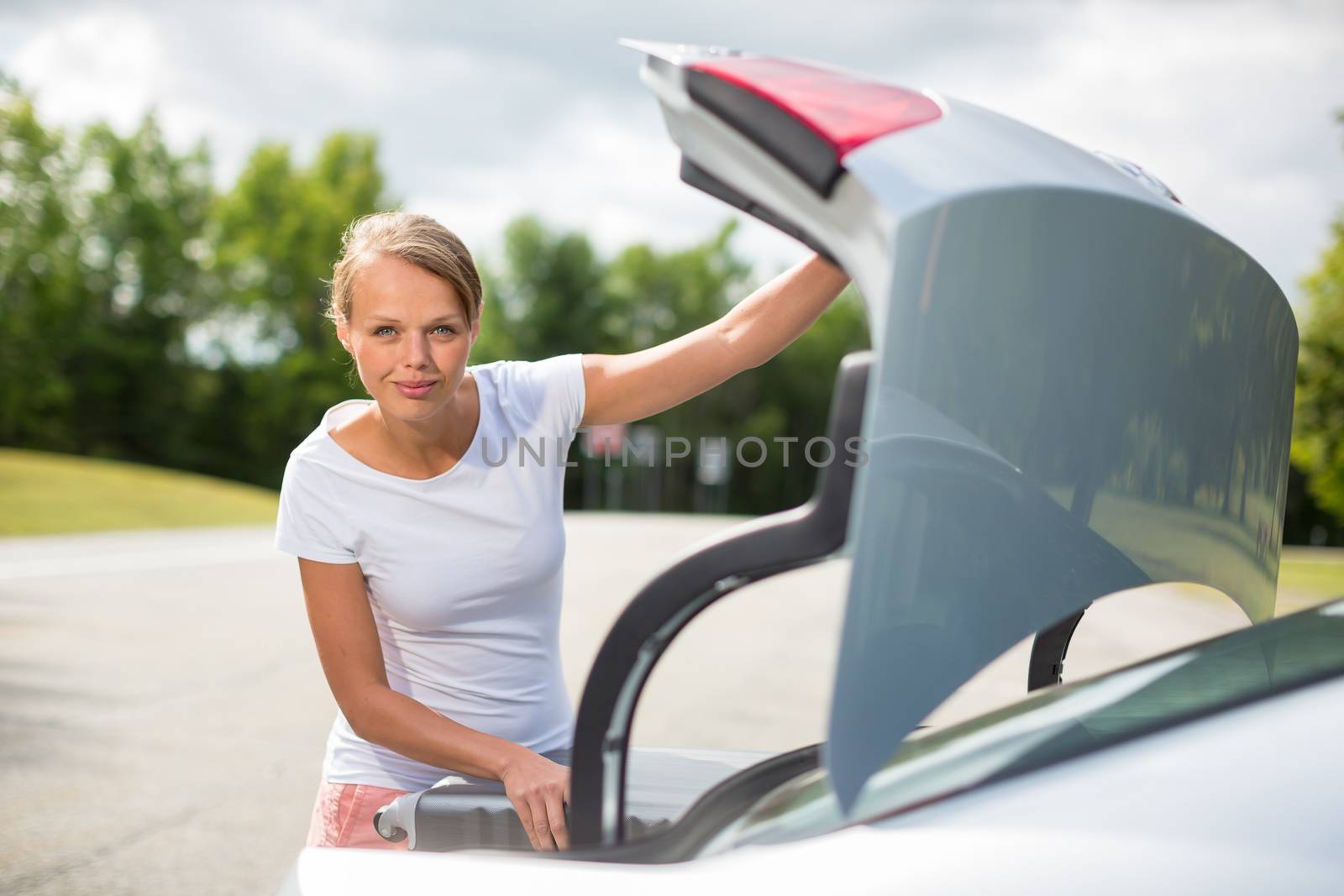 Young, attractive, happy woman taking a suitcase from her car's trunk, smiling, enjoying the travel experience