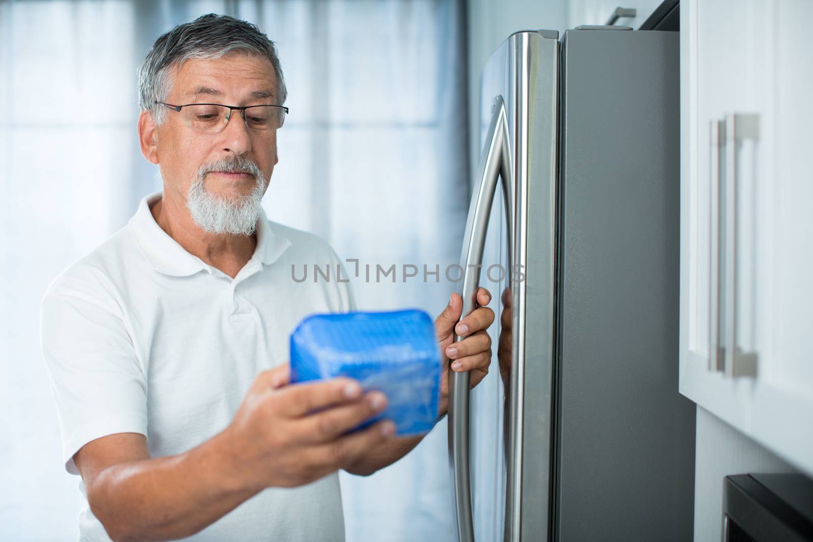Is this still fine? Senior man in his kitchen by the fridge, looking at the expiry date of a product she took from her fridge -