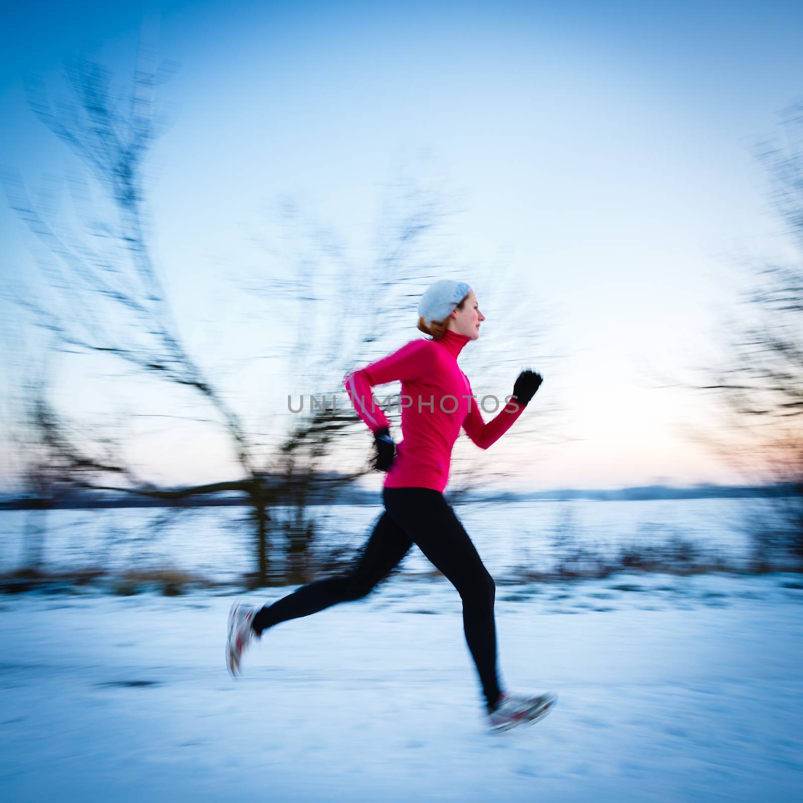 Winter running - Young woman running outdoors on a cold winter day (motion blurred image, color toned image)