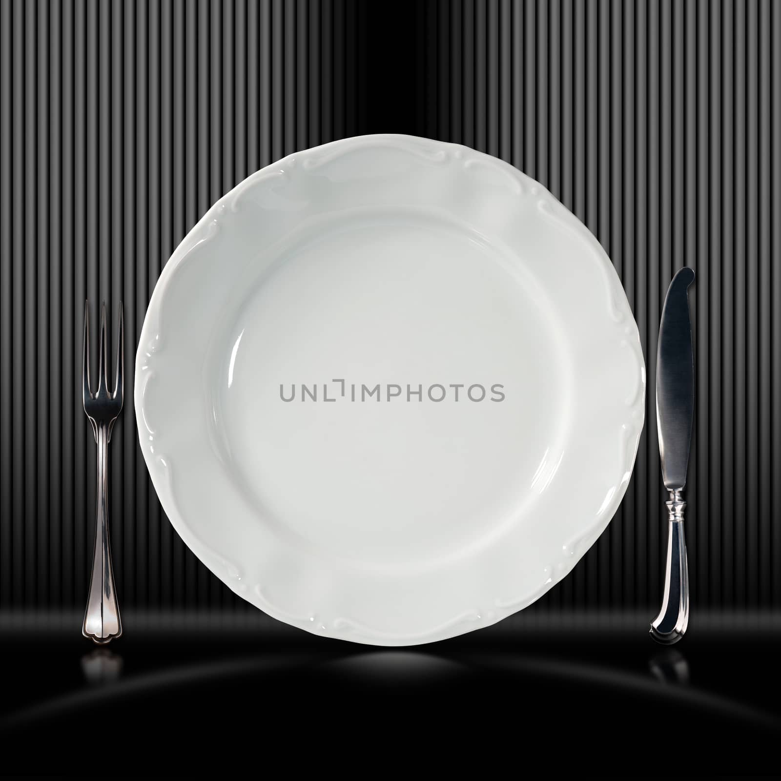 Empty and white plate on black and grey corrugated background with silver cutlery, fork and knife