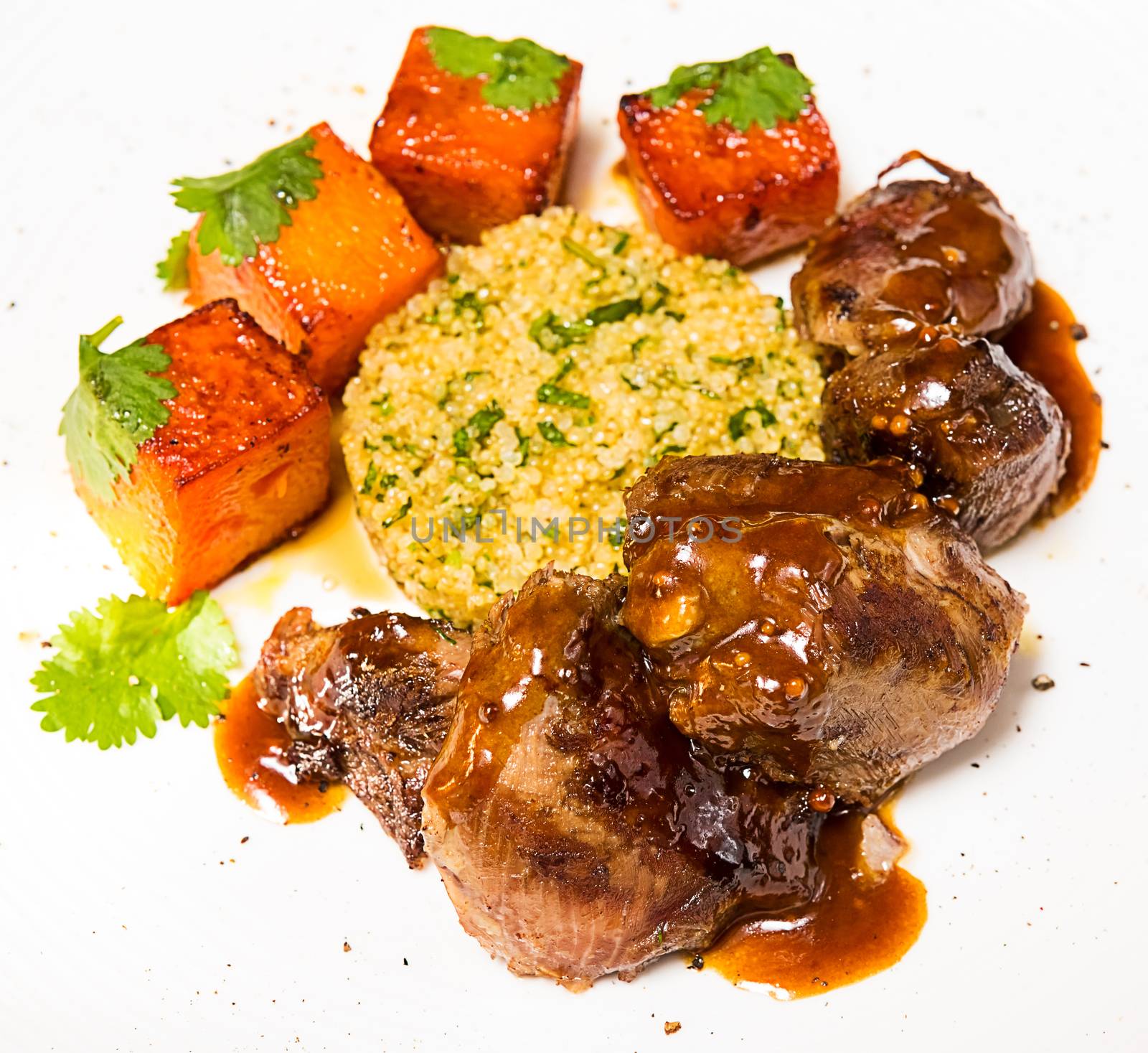 Organic meat of lamb cooked with slices of pumpkin and quinoa in oriental style on a white plate