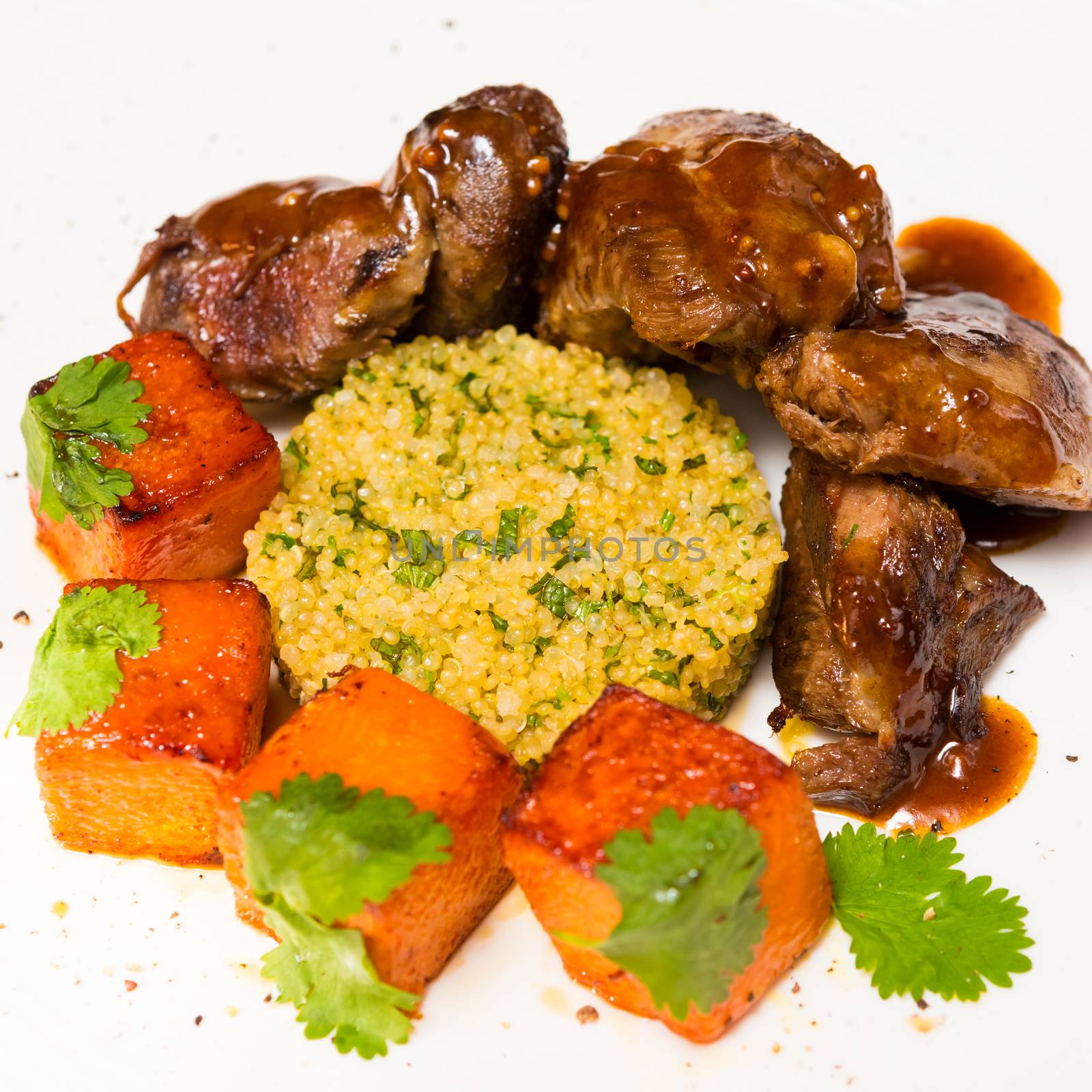 Organic meat of lamb cooked with slices of pumpkin and quinoa in oriental style on a white plate