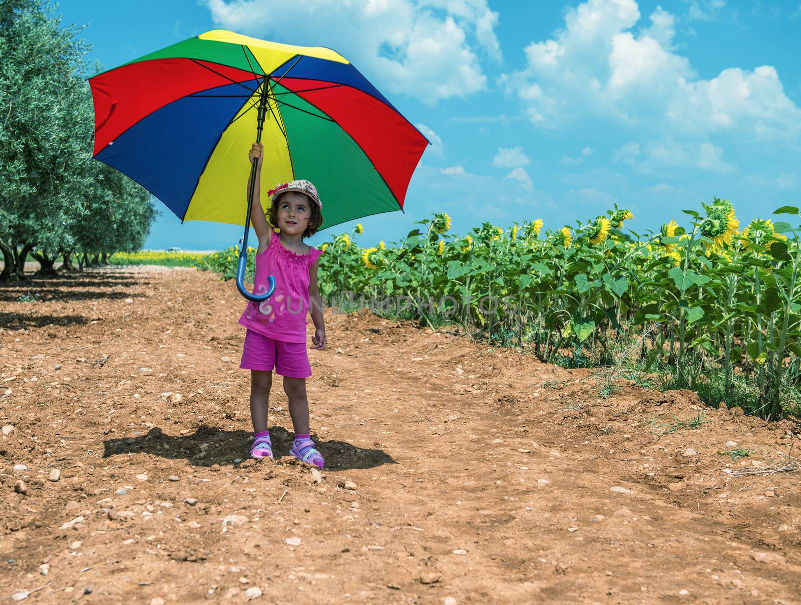 Baby girl enjoying outdoor with colorful umbrella and sunflowers by jovannig