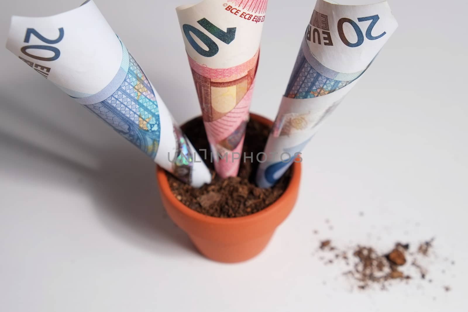 Overview of three Euro Banknotes planted in a clay pot growing out. Isolated objects with debris on the table surface