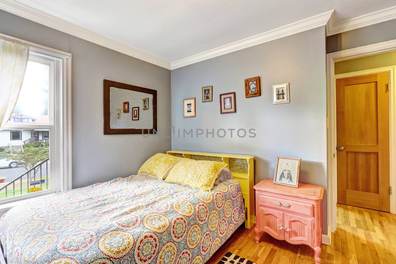 Simple bedroom with light blue walls. Bed decorated with yellow pillows. Antique pink nightstand