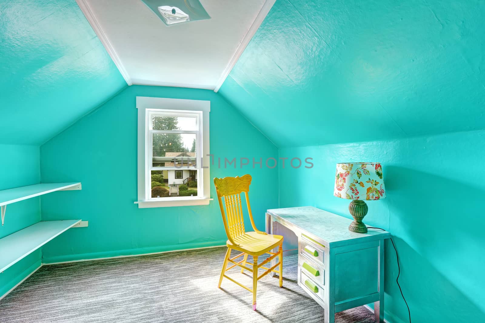 Small bright turquoise room with vaulted ceiling and shelves attached to the wall. Room has desk and chair