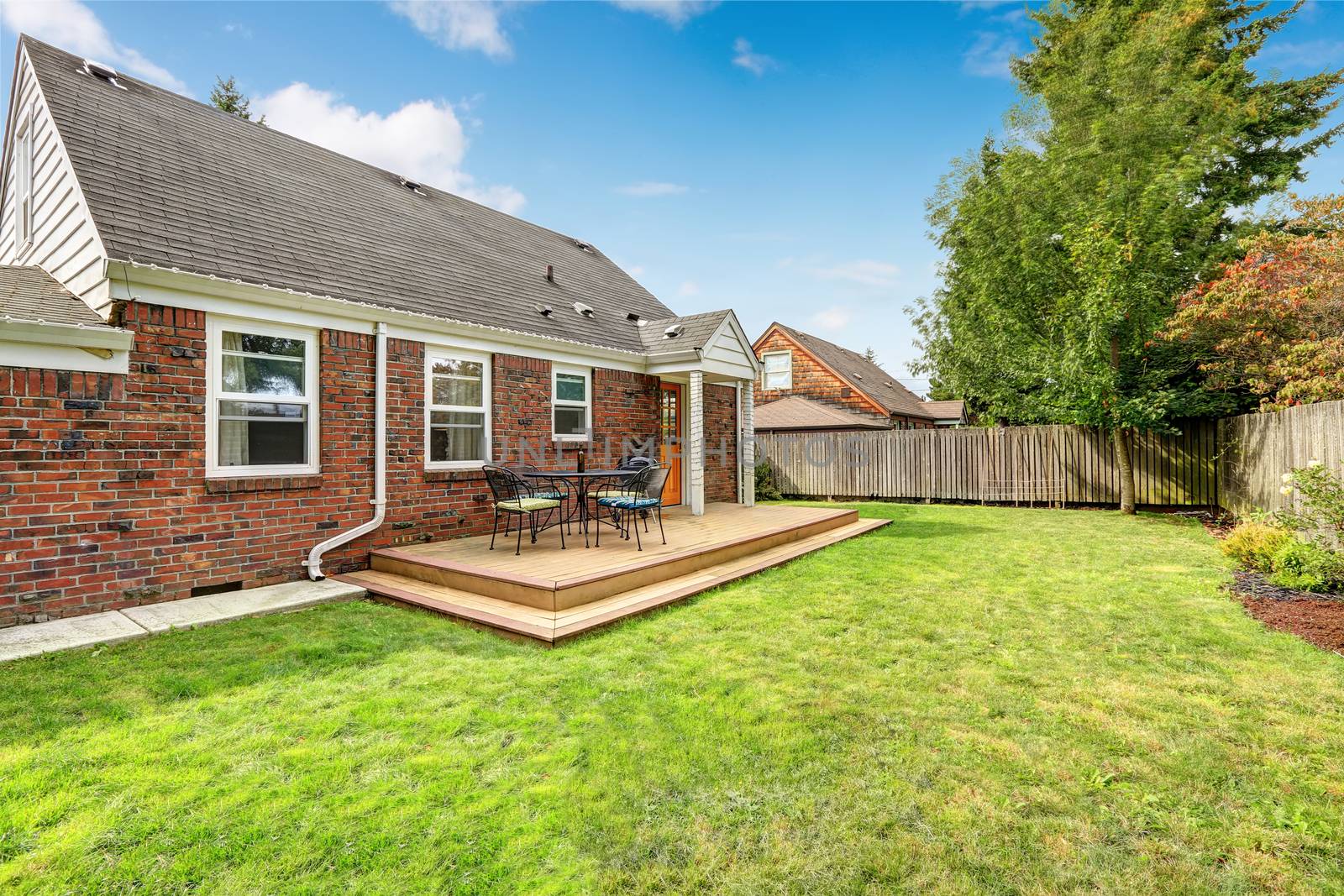 Brick house exterior with walkout wooden deck and patio area with barbecue