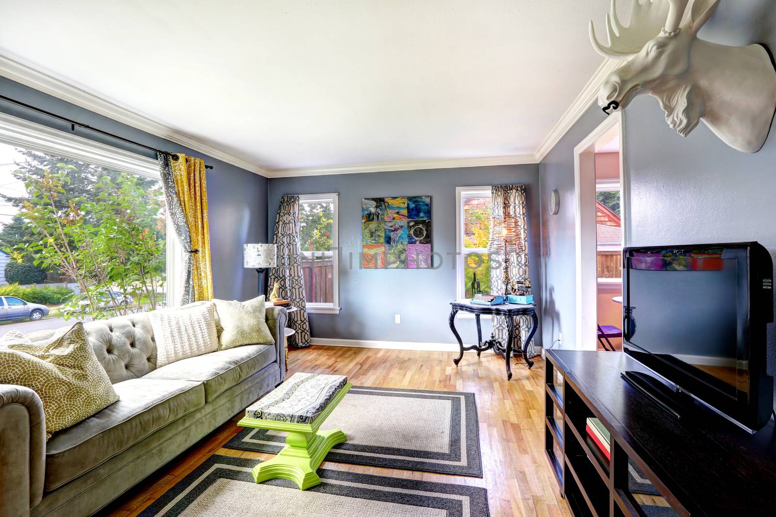 Bright living room interior with large window. Furnished with sofa, cabinet with tv and table in the corner