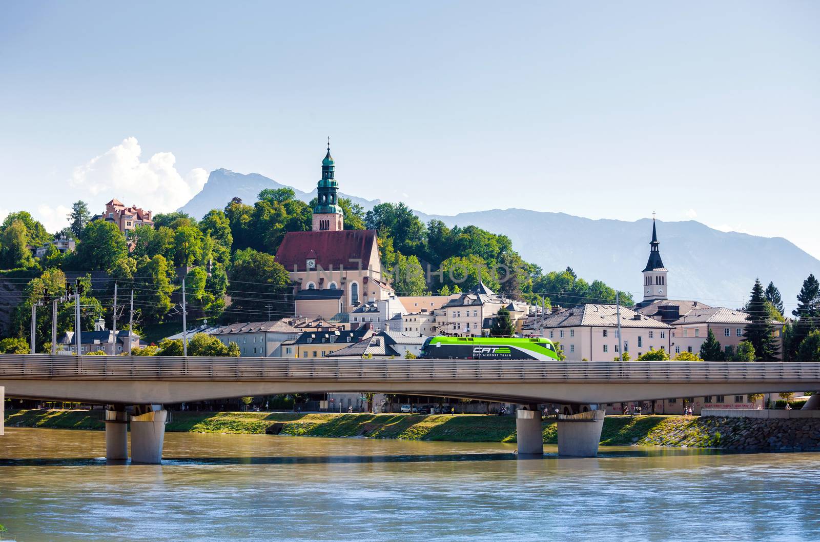Hallstatt, Austria - August 5, 2013: Electric locomotive crossing the bridge in fron of Pfarramt Mulln catholic church in Salzburg, Austria.