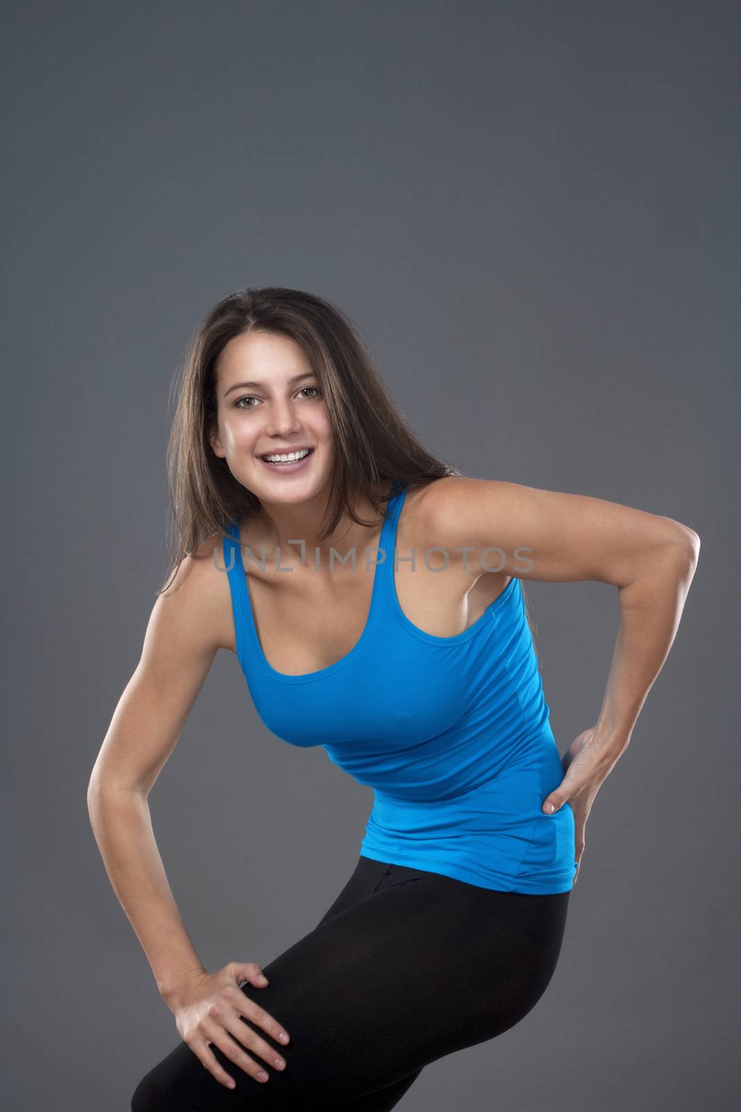 energetic young woman with blue top dancing - isolated on gray background