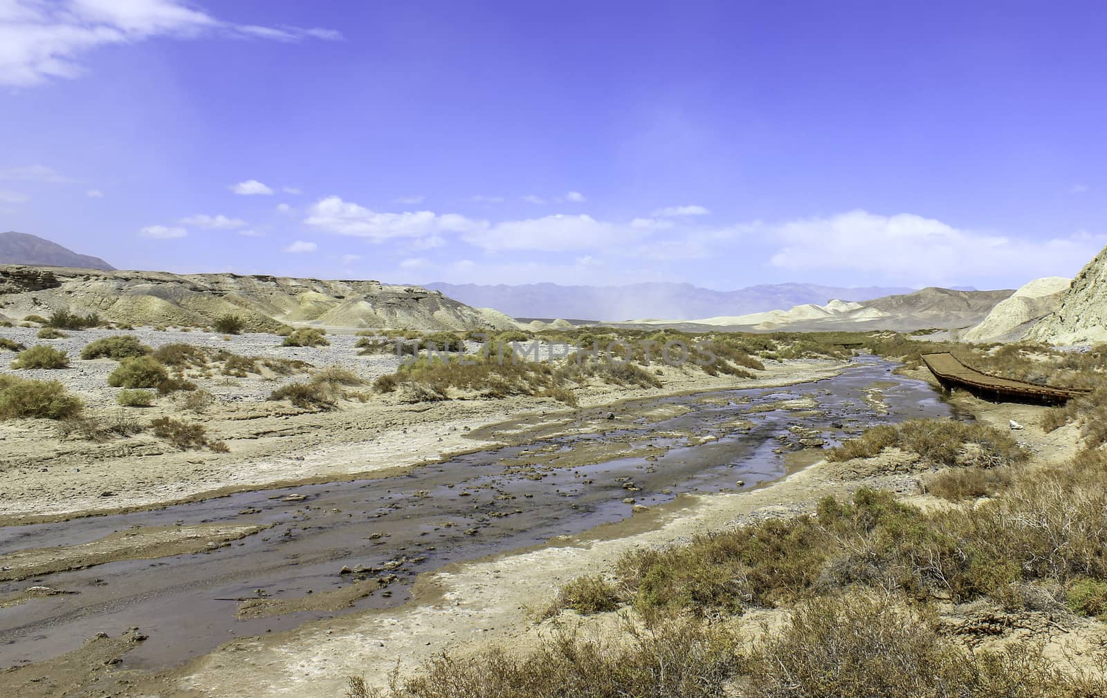 An image of a nearly dried out river with a disused wooden bridge and mountains in the distance