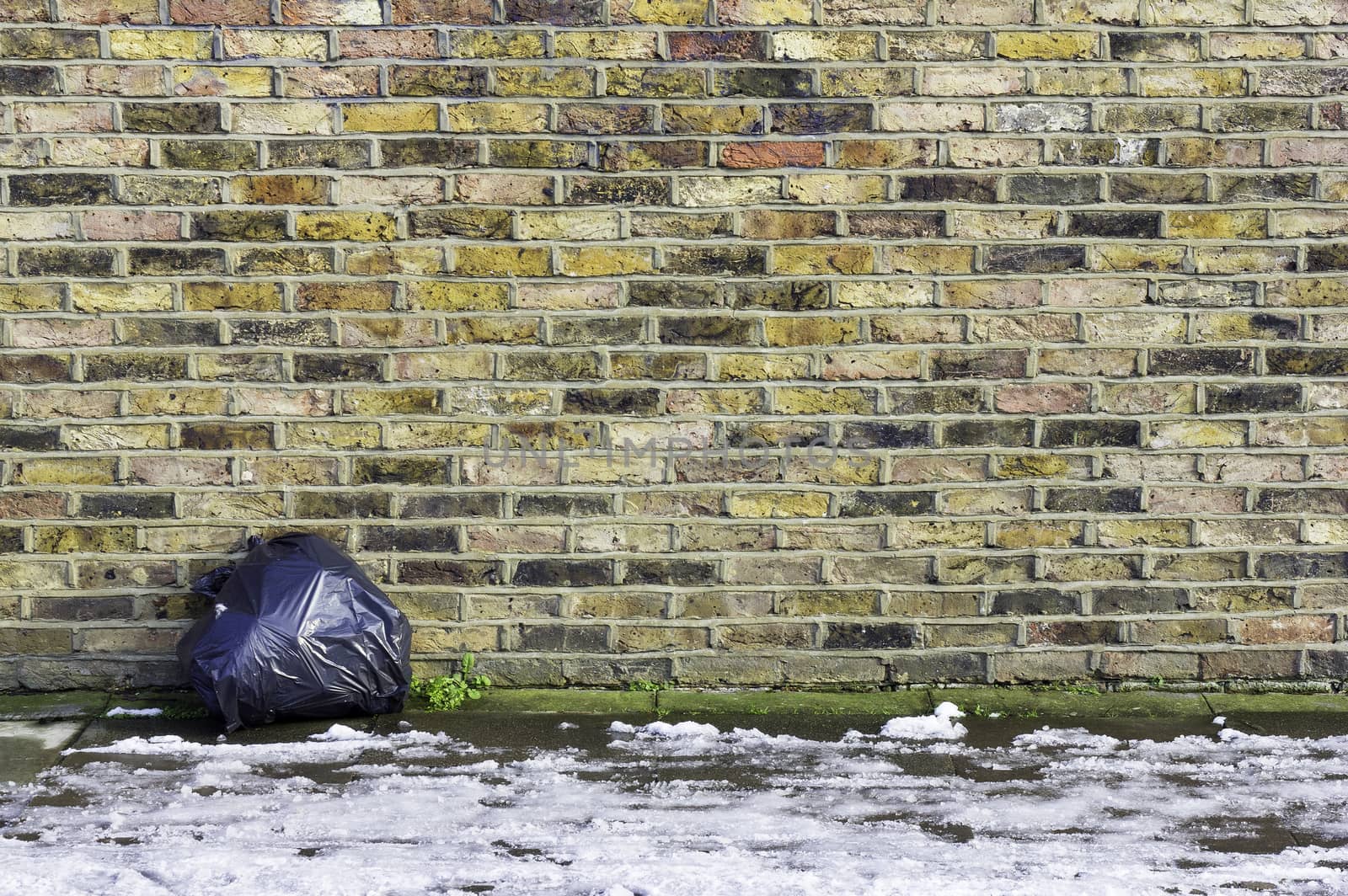 A colorful brick wall with a single black garbage sack left leaning against it