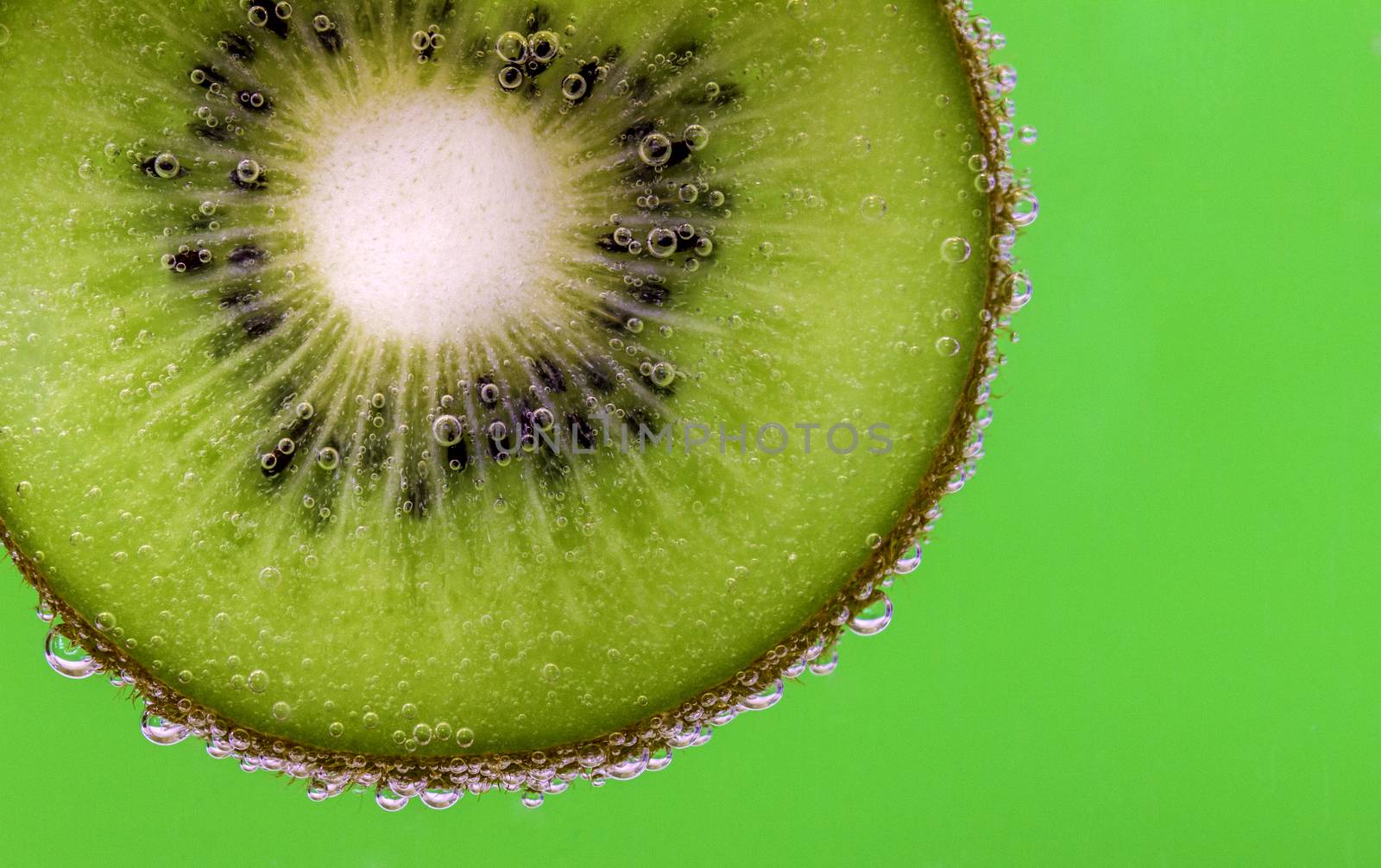 Closeup of a kiwi slice covered in water bubbles against a green background