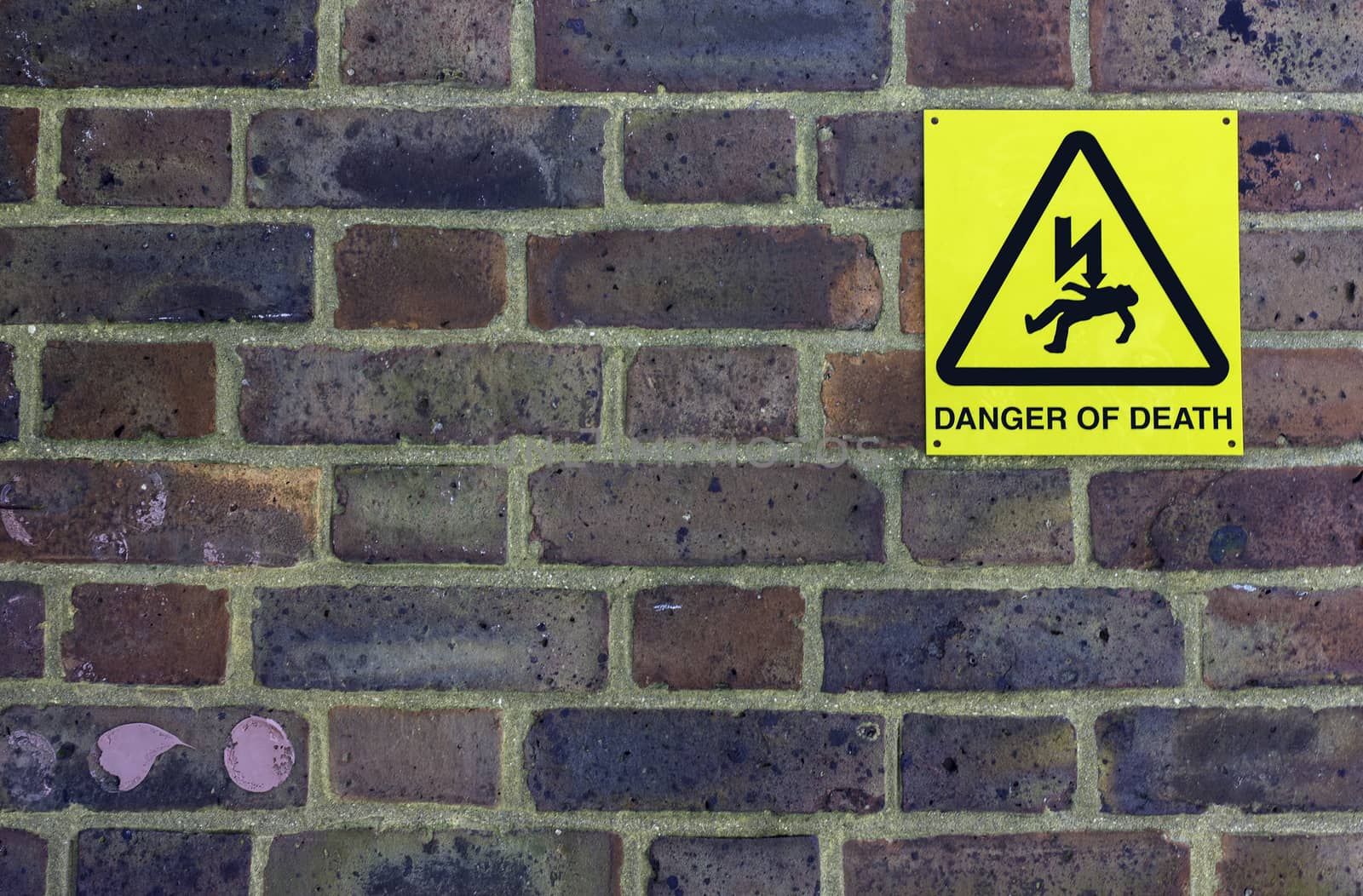 A colorful brick wall with a 'Danger of Death' sign and pink bubblegum stuck to it