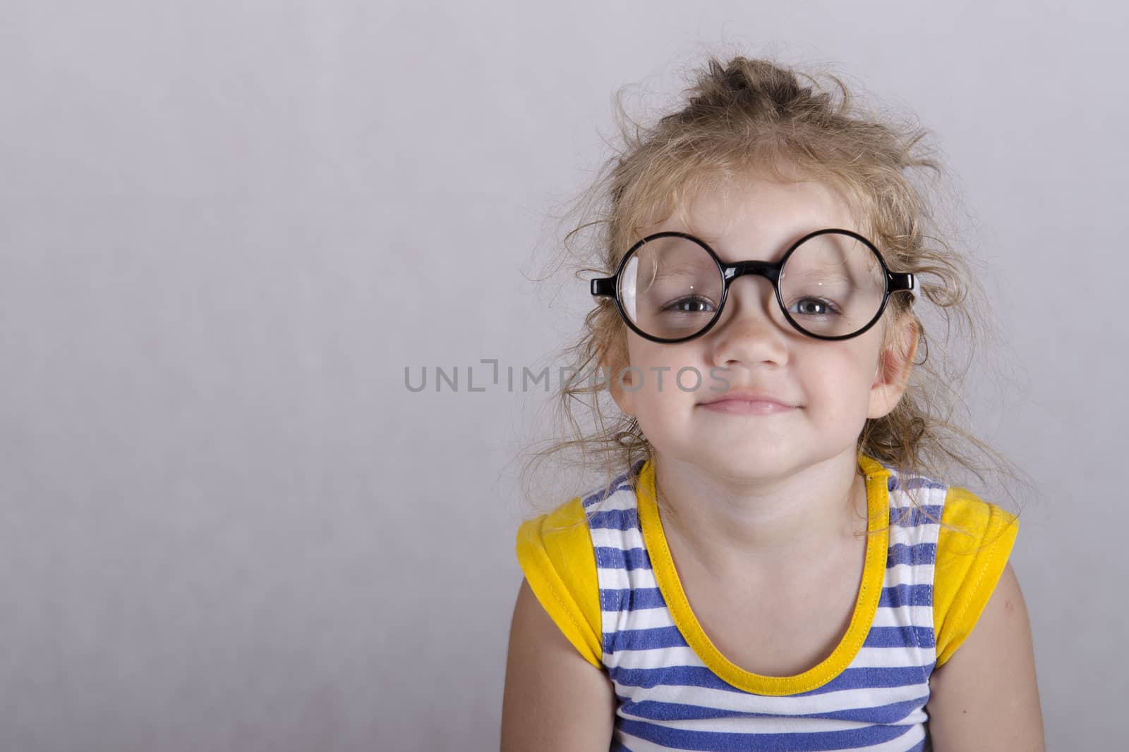 Studio, two-year-old girl sitting on the table, covered with a white cloth, and looking at the picture. Girl dressed funny glasses, hands laid on my knees