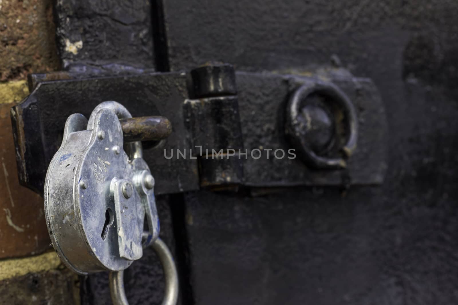 A close up of a strong looking silver padlock on a black metal door