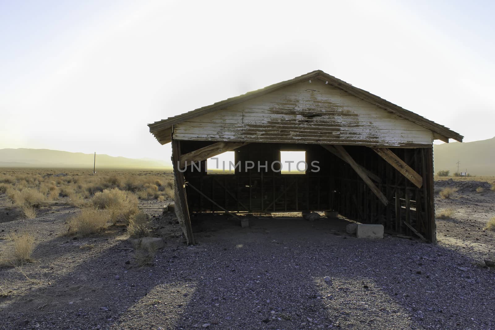 A deserted old rickety hut or shed leaning to one side in the desert with the setting sun creating a silhouette behind