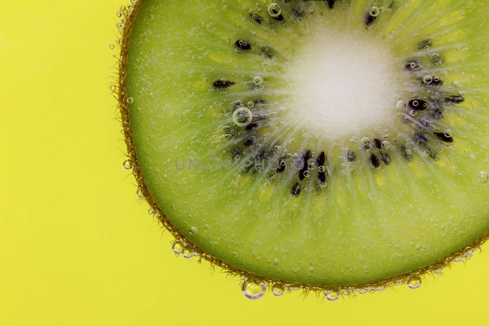Closeup of a kiwi slice covered in water bubbles against a yellow background
