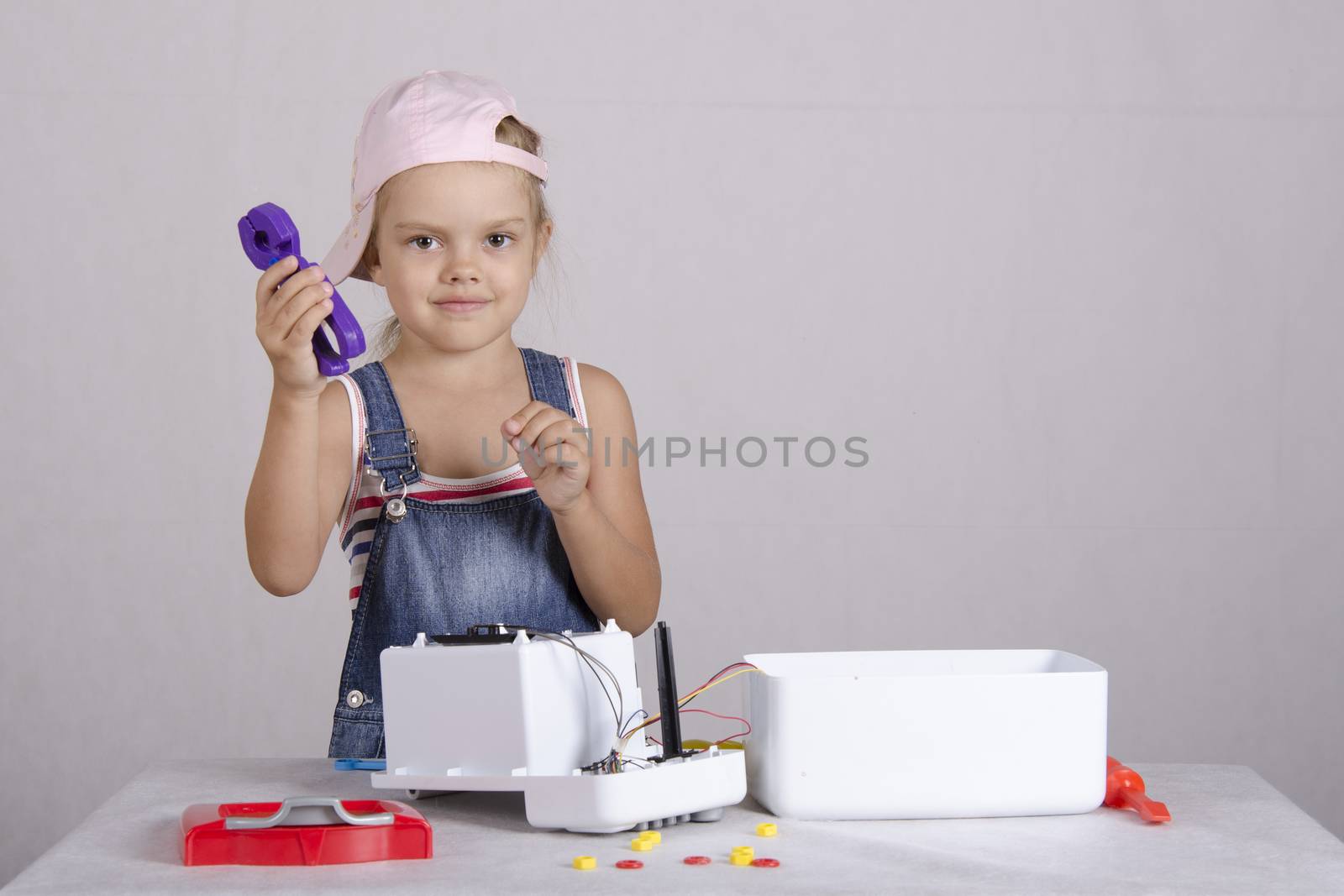 Girl playing in the repairer and repairs toy microwave. Girl Holding a pair of pliers, and looks in the frame