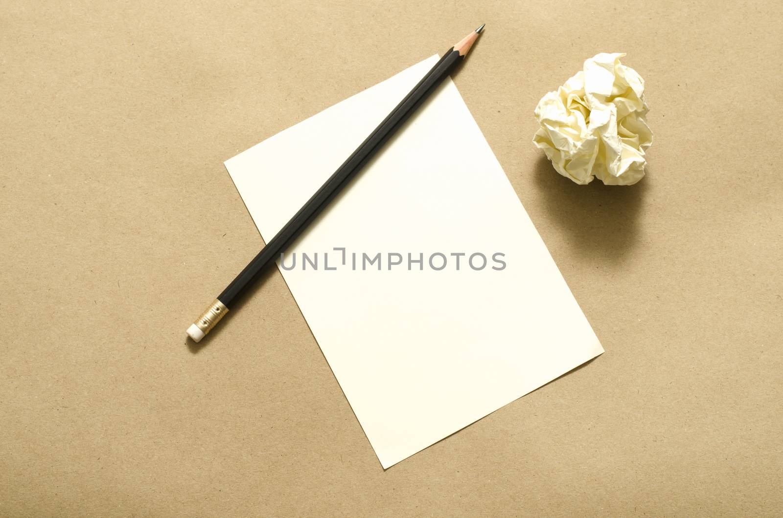 Pencil on clear white paper with crumble paper balls on brown color background