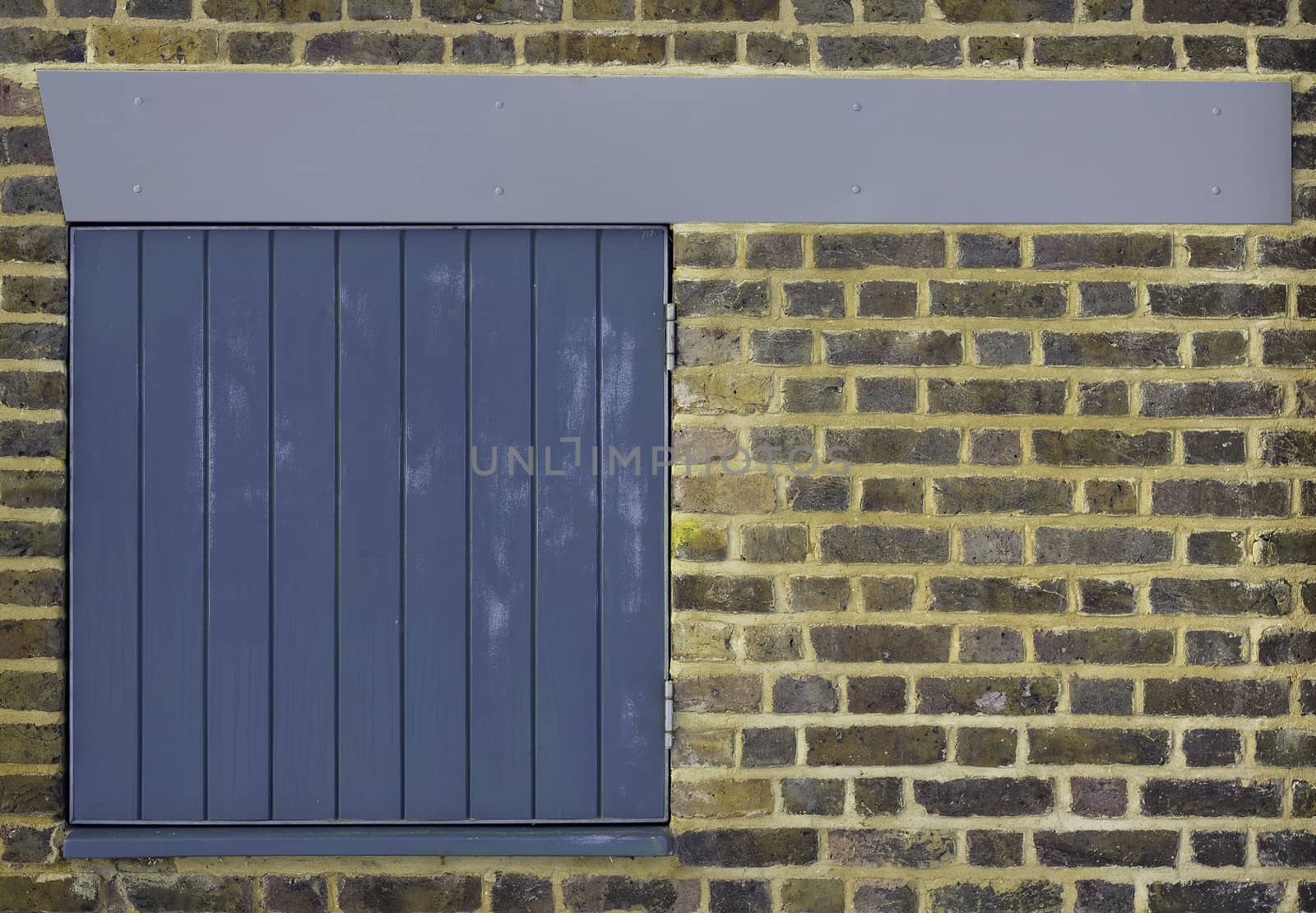A clean brick wall with a small blue slatted door hatch and pleasing blue/grey beam across the top