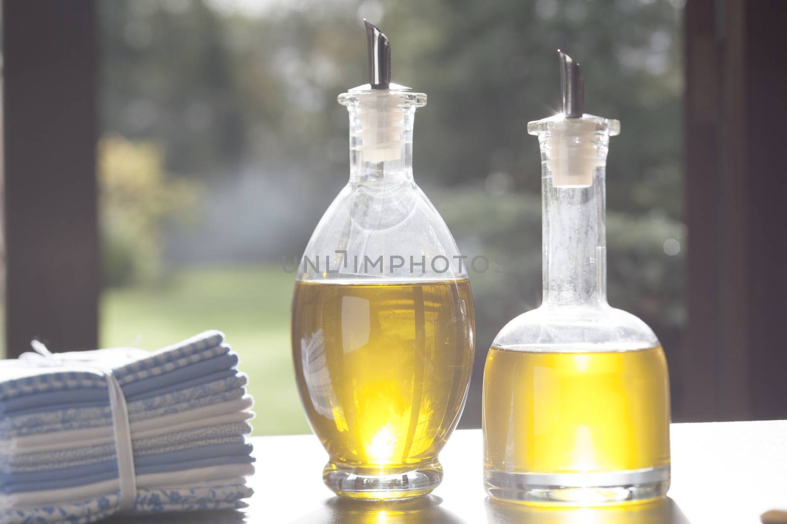 Two bottles of olive oil on table in front of window.