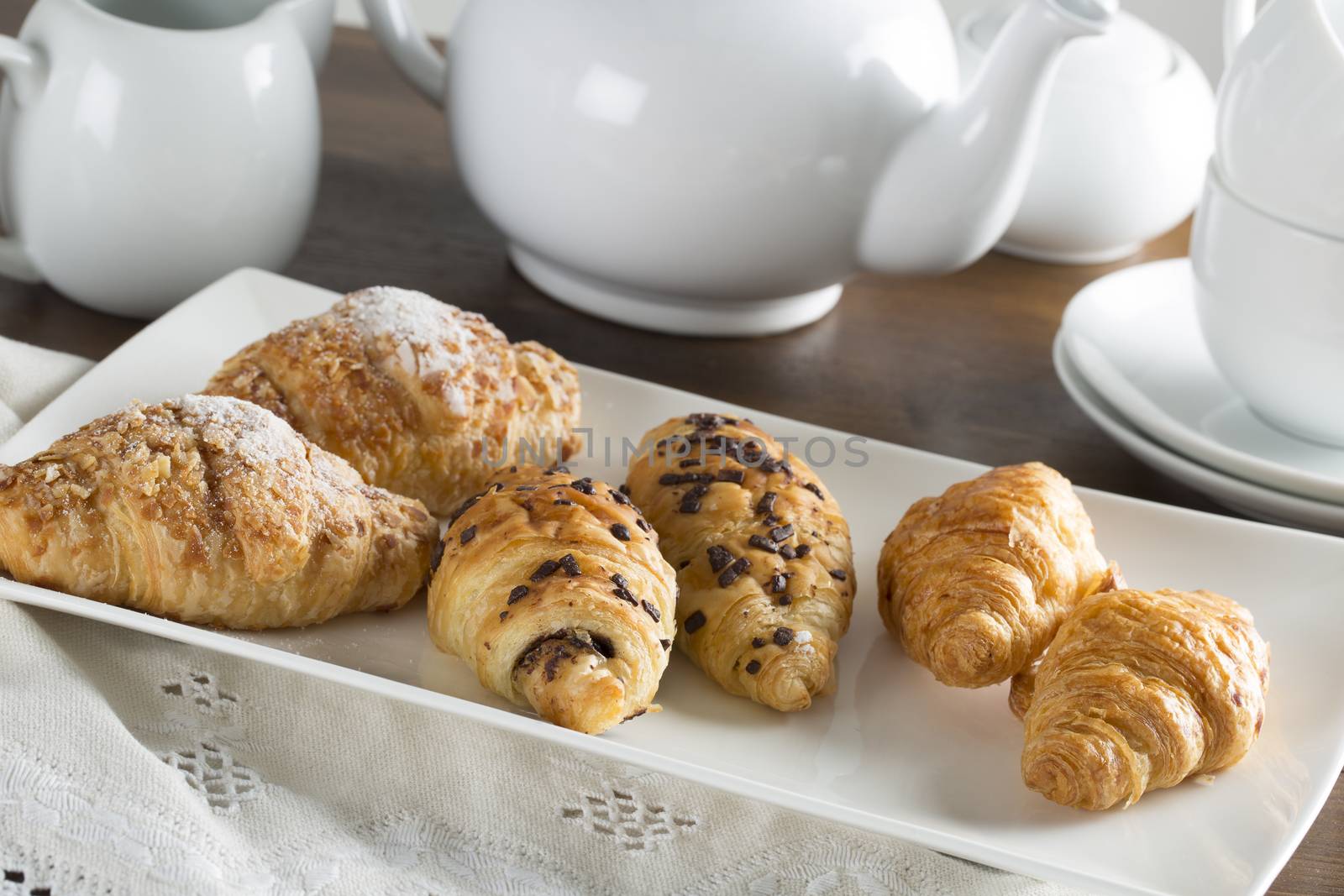 Morning croissants on serving plate with tea pot in background