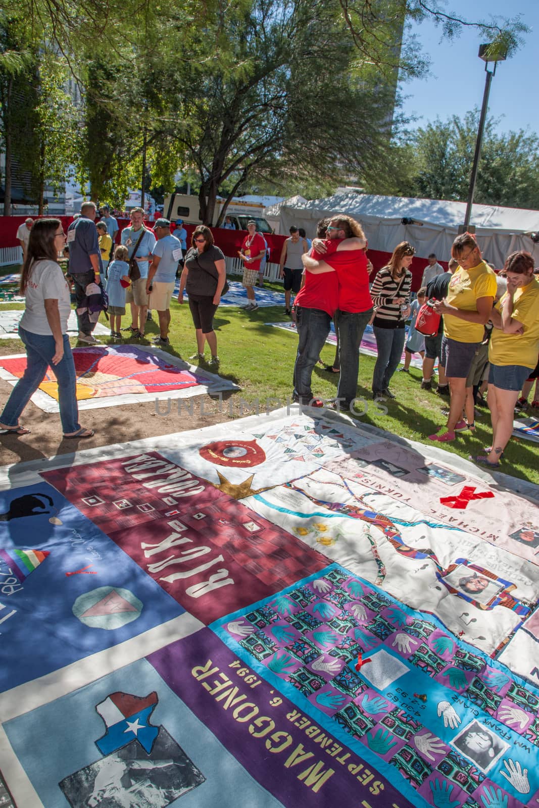 People Hugging Near Section of AIDS Quilt by Creatista