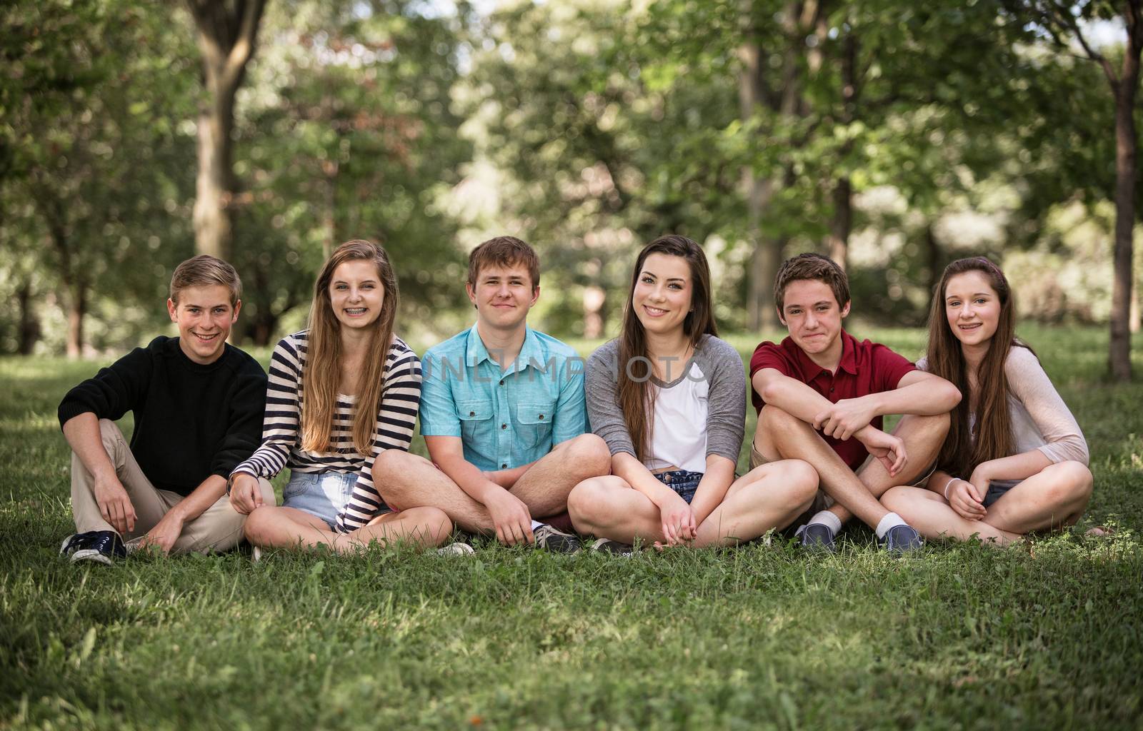 Group of six teens sitting outdoors on grass