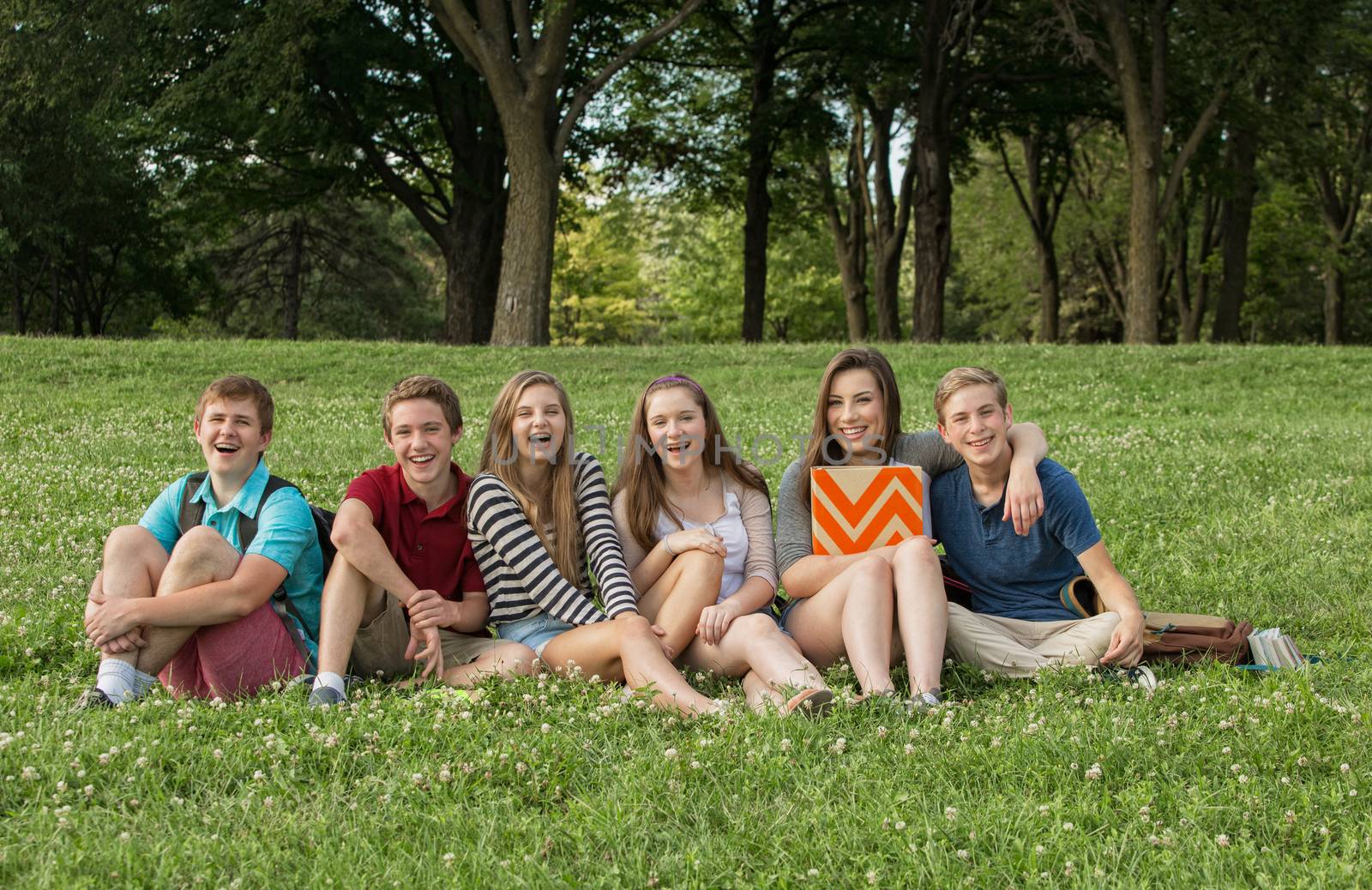 Cheerful teen students sitting outdoors on grass