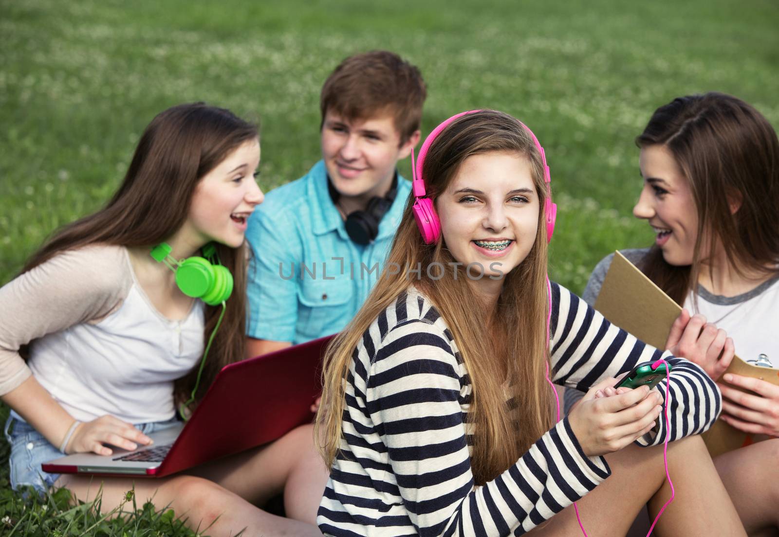 Cute teen with friends sitting outdoors on lawn