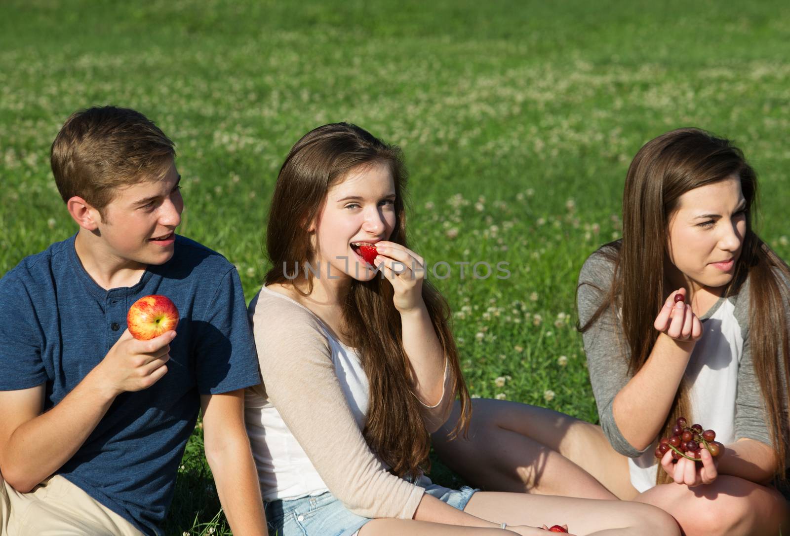 Trio of happy Caucasian teenagers eating fruit outdoors
