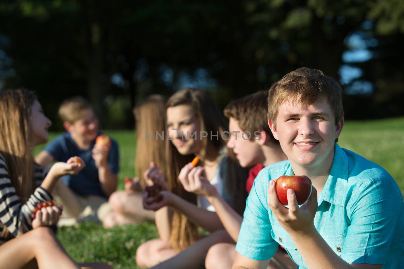 Cute European teen boy with friends holding apple