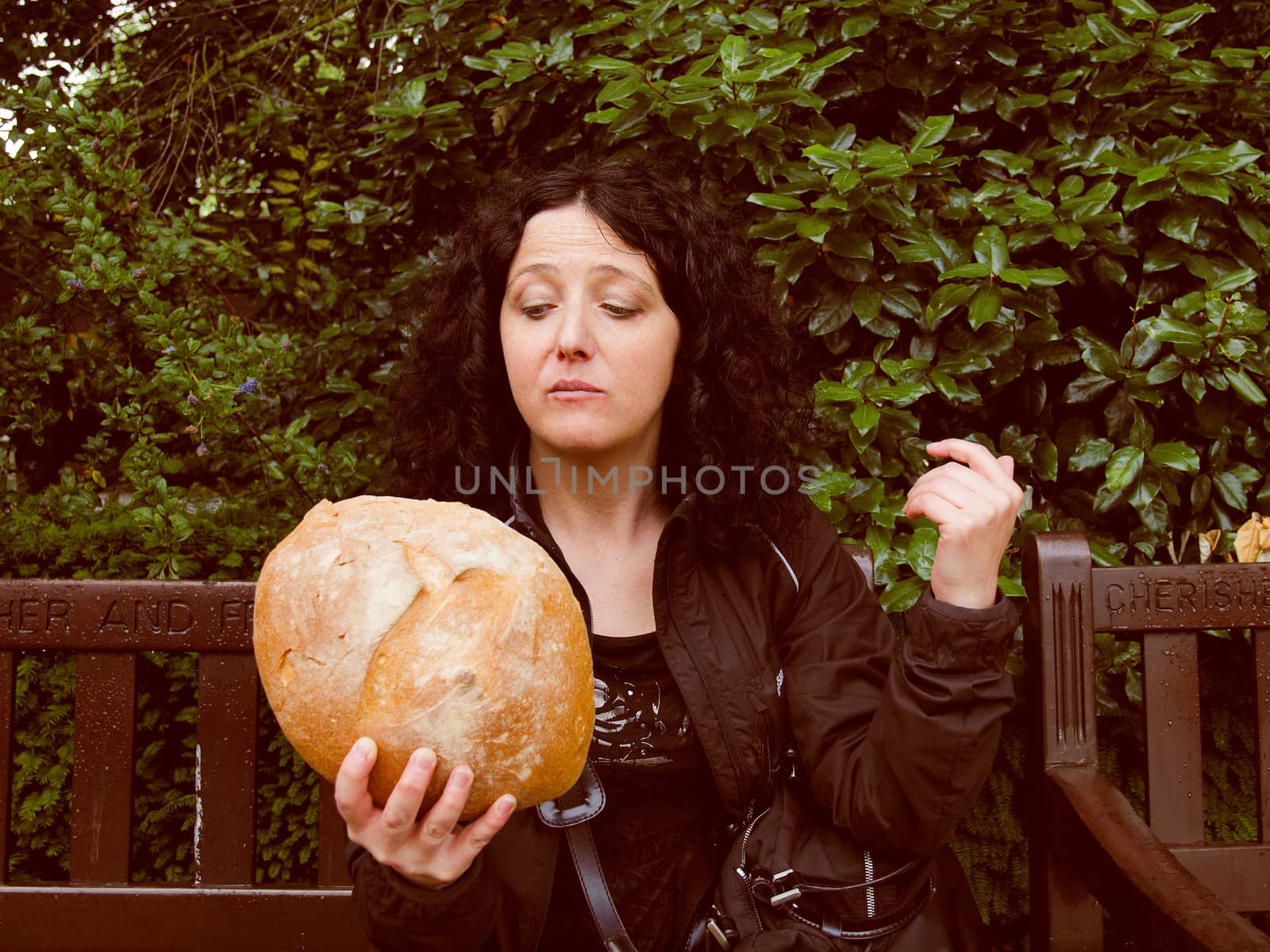 Portrait of pretty young brunette looking at huge bread in hamletic pose - To eat or not to eat