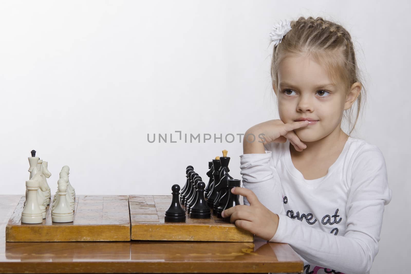 The girl sitting at the table, on which stands the chess Board. The girl thought for a moment and slyly looked to the left