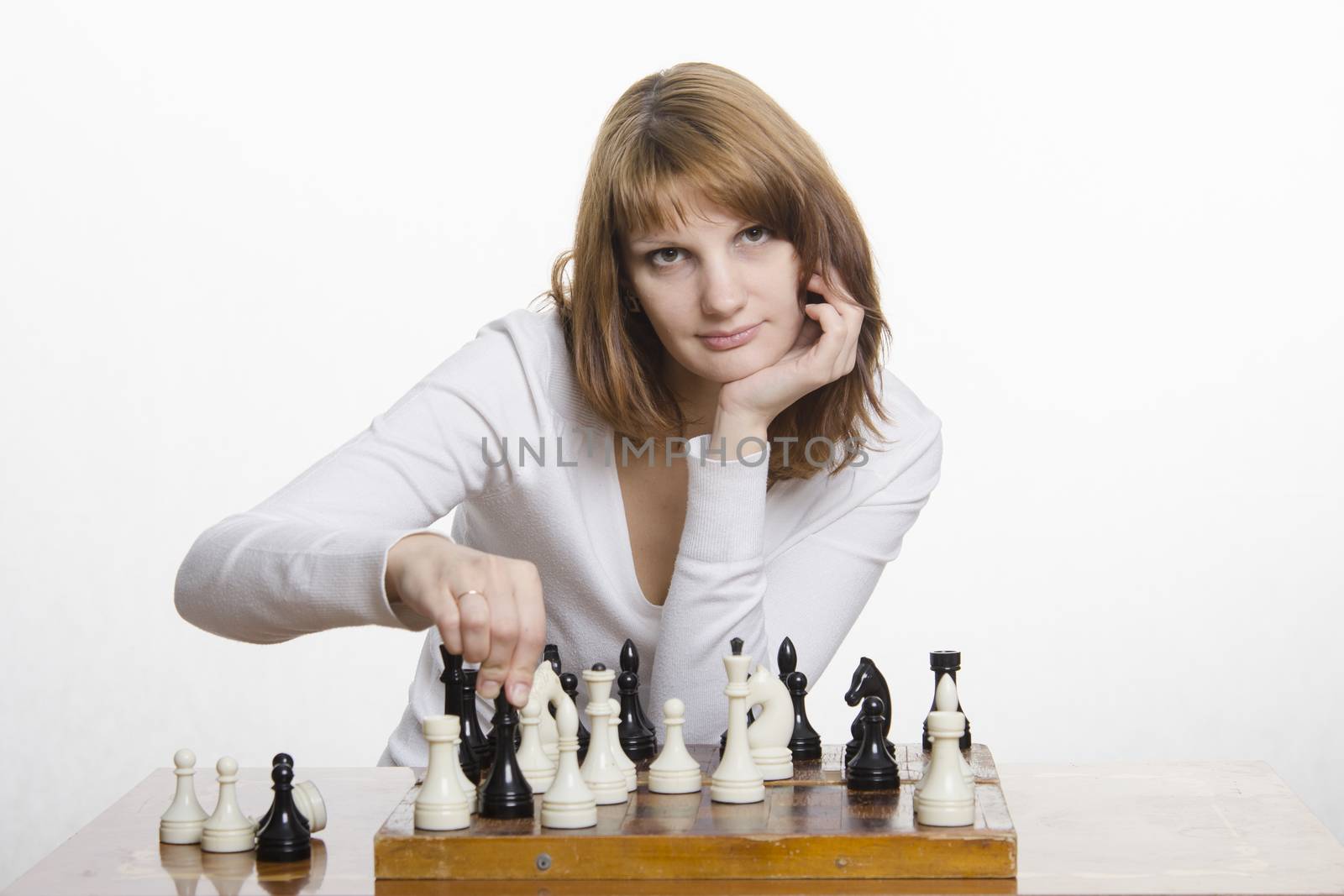 Young girl playing chess. Girl walks figure and looks into the frame