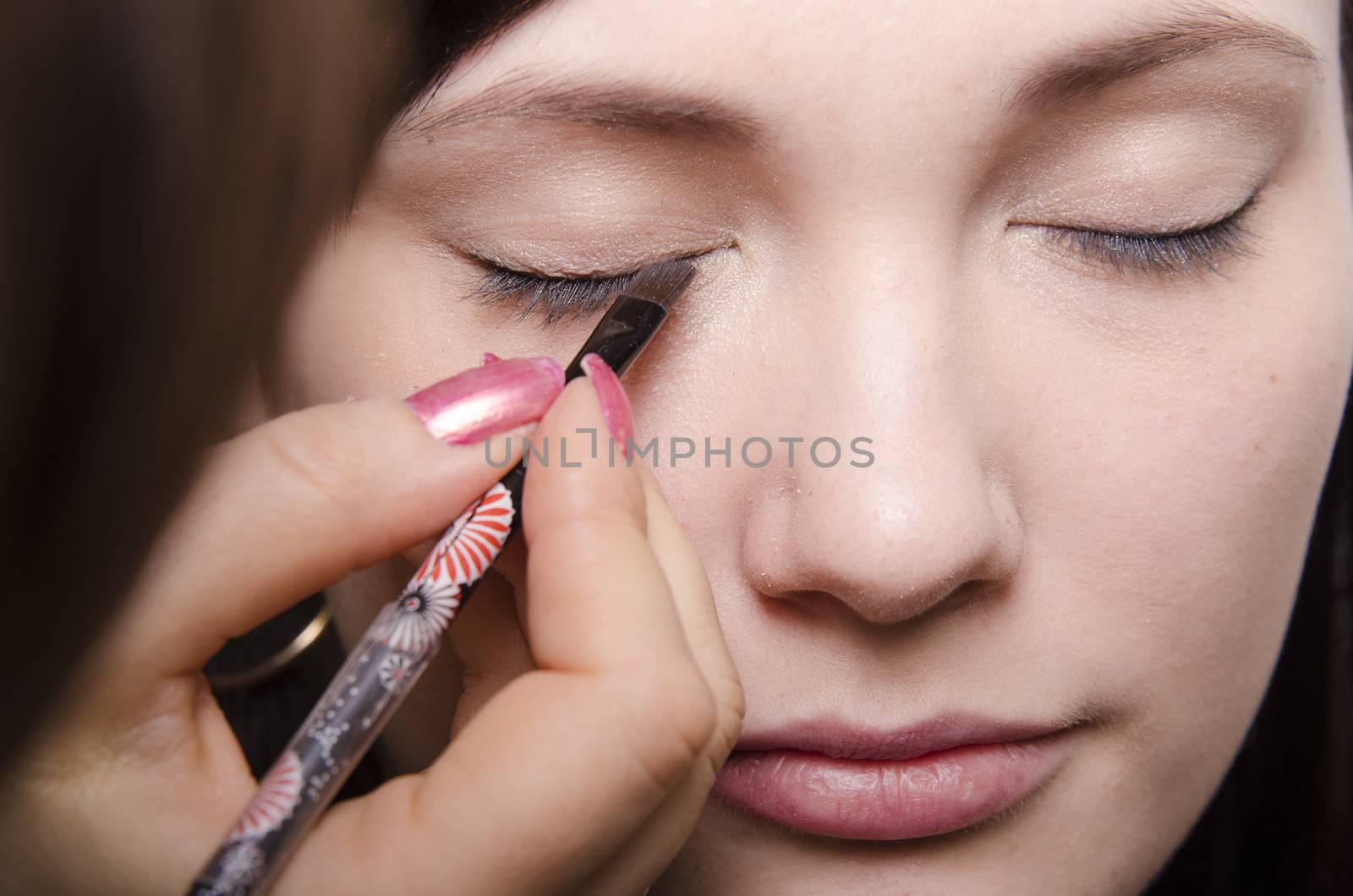 Makeup artist deals makeup on the model's face. She paints eyelashes model.